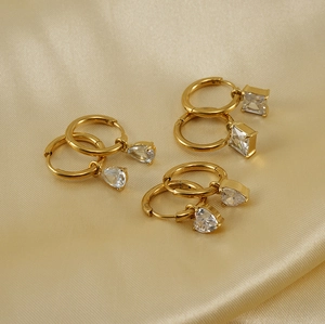 Close-up of 18K gold earrings set with heart, drop, and square zircon on silk fabric