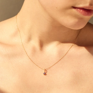 Detail of minimalist gold chain with a round purple zircon pendant on collarbone