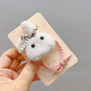 Detail of plush white rabbit hair tie with a brown checkered bow on a pink card
