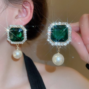 Detail of vintage palace style earrings with emerald-cut green stone and white pearl