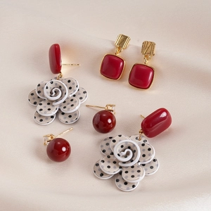 Detailed view of red resin flower and geometric earrings on soft beige fabric