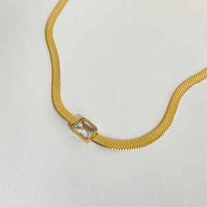 Close-up of golden herringbone chain with a clear rectangular gemstone pendant