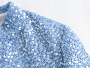 Close-up of light blue tweed jacket showing silver sequins and woven texture detail