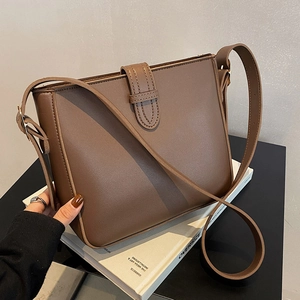 Chic brown PU leather bucket bag with flap closure and adjustable strap on a book stack
