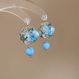 Detail of floral butterfly earrings featuring blue crystal stones and pearl beads on gold