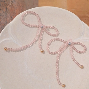 Detailed close-up of handmade pink beaded crystal bow charm in a ceramic bowl