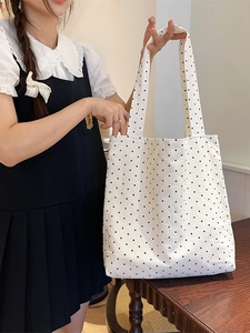 Minimalist white canvas tote bag with black polka dots shown in a cozy indoor setting