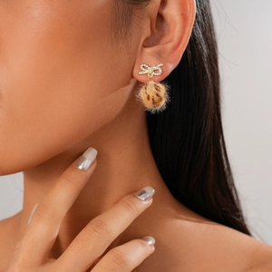 Close-up of golden bow rhinestone earrings with brown animal print fur ball pendants