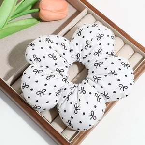 Macro view of white floral scrunchie with black bows and dots in a wooden tray