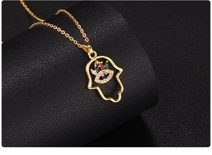 Macro shot of gold-plated Hamsa hand pendant with colorful zircons on black background