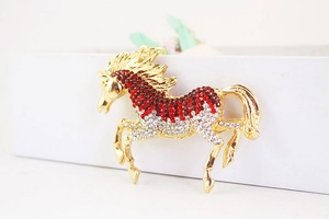 Close-up of golden horse keychain featuring red and clear rhinestones on a white box