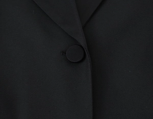 Détail de veste noire montrant le bouton recouvert et la texture du tissu tissé