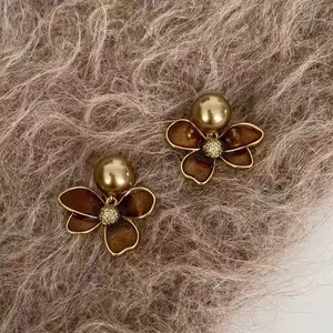 Detailed view of flower-shaped earrings with brown petals and faux pearl on fur background