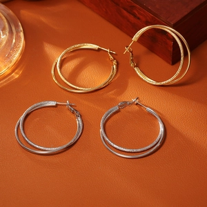 Macro detail of textured gold and silver double-layered round hoop earrings on orange base