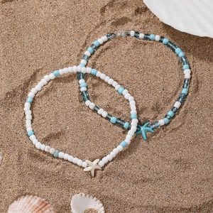 Detail of beaded shell anklets with starfish charms on sandy beach background