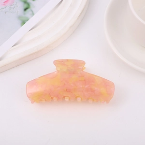 Dettaglio macro di un fermaglio per capelli in acetato con trama marmorea rosa e arancio