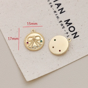 Macro detail of round gold-plated bow pendant with gemstones measuring 15mm by 17mm