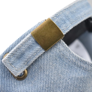 Detailed macro view of the adjustable bronze metal buckle on a washed denim baseball cap