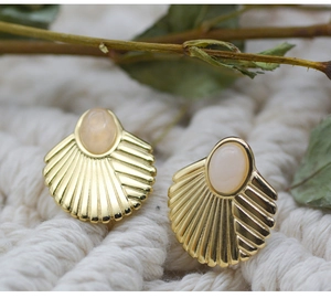 Macro shot of gold-plated fan-shaped shell earrings with inlaid oval gemstone detail