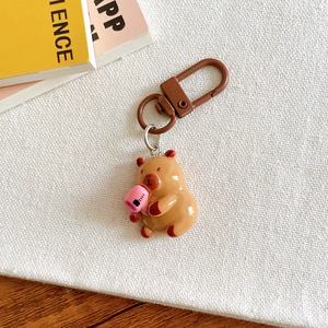 Detailed close-up of a brown capybara keychain holding a pink drink on white fabric
