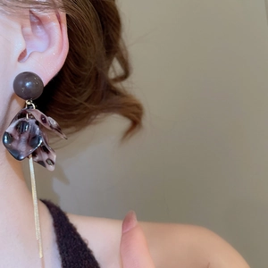 Détail des boucles d'oreilles feuilles de ginkgo en acrylique avec pompons dorés sur modèle