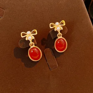 Vintage bow earrings with pearls and red oval resin stones on a velvet jewelry stand