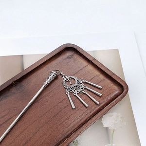 Detailed view of silver ethnic hair pin with moon crescent and tassels on wooden tray