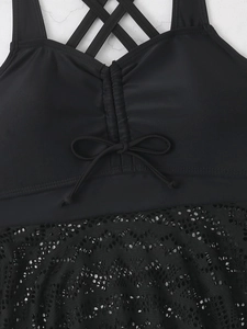 Detail of black swimsuit with lace trim, criss-cross straps and front bow tie design