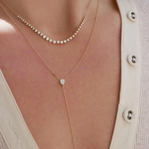 Detail of layered gold-plated Y-necklace featuring an emerald drop pendant and diamond accents