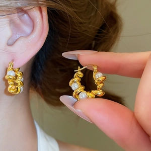 Nahaufnahme eleganter goldener gedrehter U-Ohrringe mit glänzenden weißen Perlen