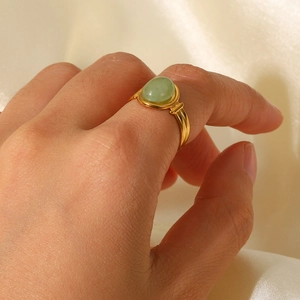 Detail of gold-plated stainless steel ring with oval green stone on satin background