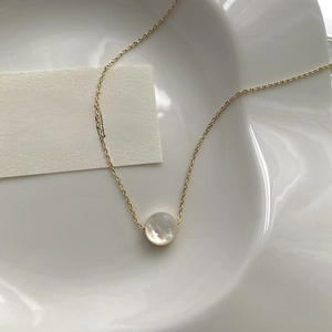 Close-up of golden necklace with iridescent white shell pendant on a white ceramic plate
