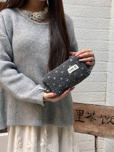 Close-up of soft grey plush pencil case with white dots held by a model in a street setting