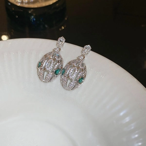 Macro detail of silver snake earrings with white zircons and green marquise gems