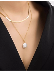 Close-up of double-layered gold snake chain necklace with baroque pearl on female model