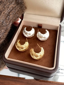 Detailed macro view of gold and silver C-shaped earrings with cross-weave texture in a gift box