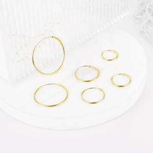 Various sizes of polished gold hoop earrings arranged on a white marble platform