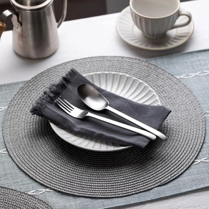 Detailed close-up of grey woven round placemat on table with elegant dinnerware