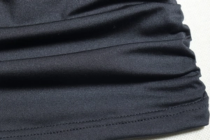 Close-up of ruched black knit fabric texture and hem stitching on a bodycon dress