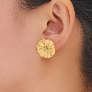 Close-up of golden sunflower pearl stud earrings worn by model to show scale and texture