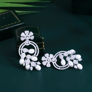 Detail of luxury flower earrings with white pearls and sparkling zircons on green fabric
