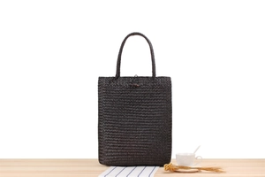 Detailed view of dark brown woven straw tote bag on a wooden table with decor