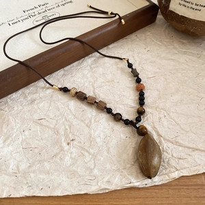 Detail view of a vintage necklace with olive stone pendant and mixed beads on a woven cord
