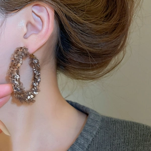 Gros plan d'un mannequin portant de grandes créoles en laine tricotée marron avec paillettes