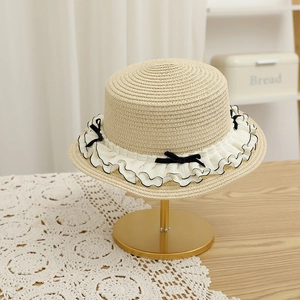 Detail view of woven straw hat featuring white pleated lace and black bows on a gold stand