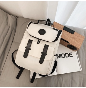 White minimalist nylon backpack featuring black leather buckle straps on a cozy bed