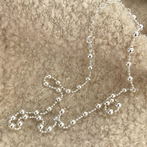 Macro detail of 925 sterling silver bead necklace with lobster clasp on beige fleece