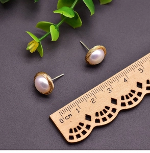 Macro shot of 10-12mm gold wire-wrapped pearl stud earrings against a dark background