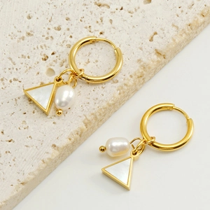 Gold hoop earrings with triangular shell and pearl pendants on beige stone background