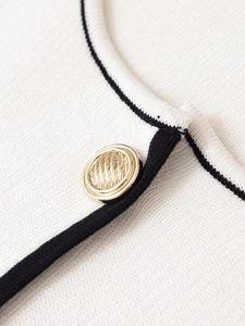 Vue macro d'un cardigan en tricot blanc avec bordure noire et bouton doré texturé